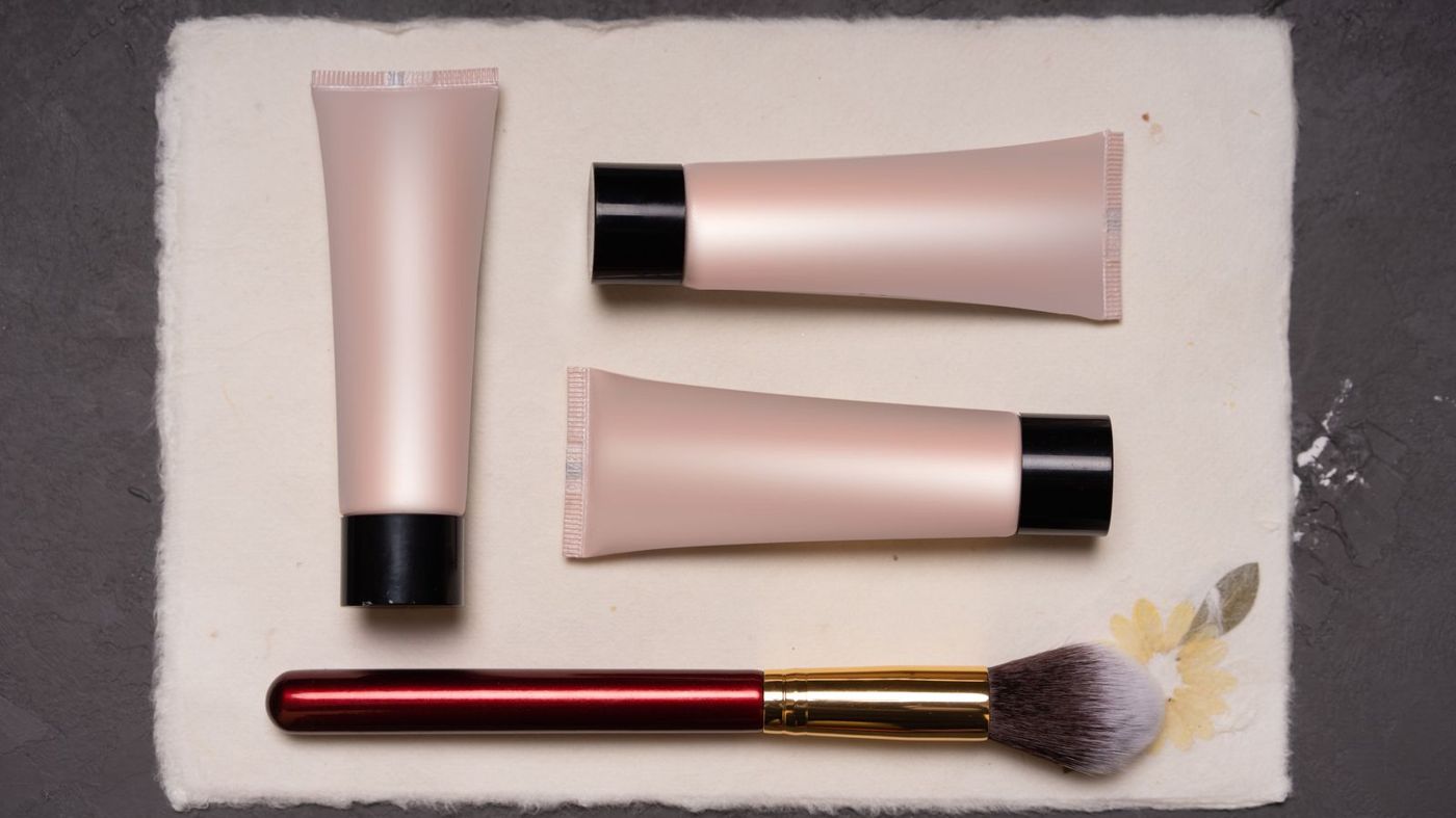 Skincare tubes and a makeup brush arranged flat on a table