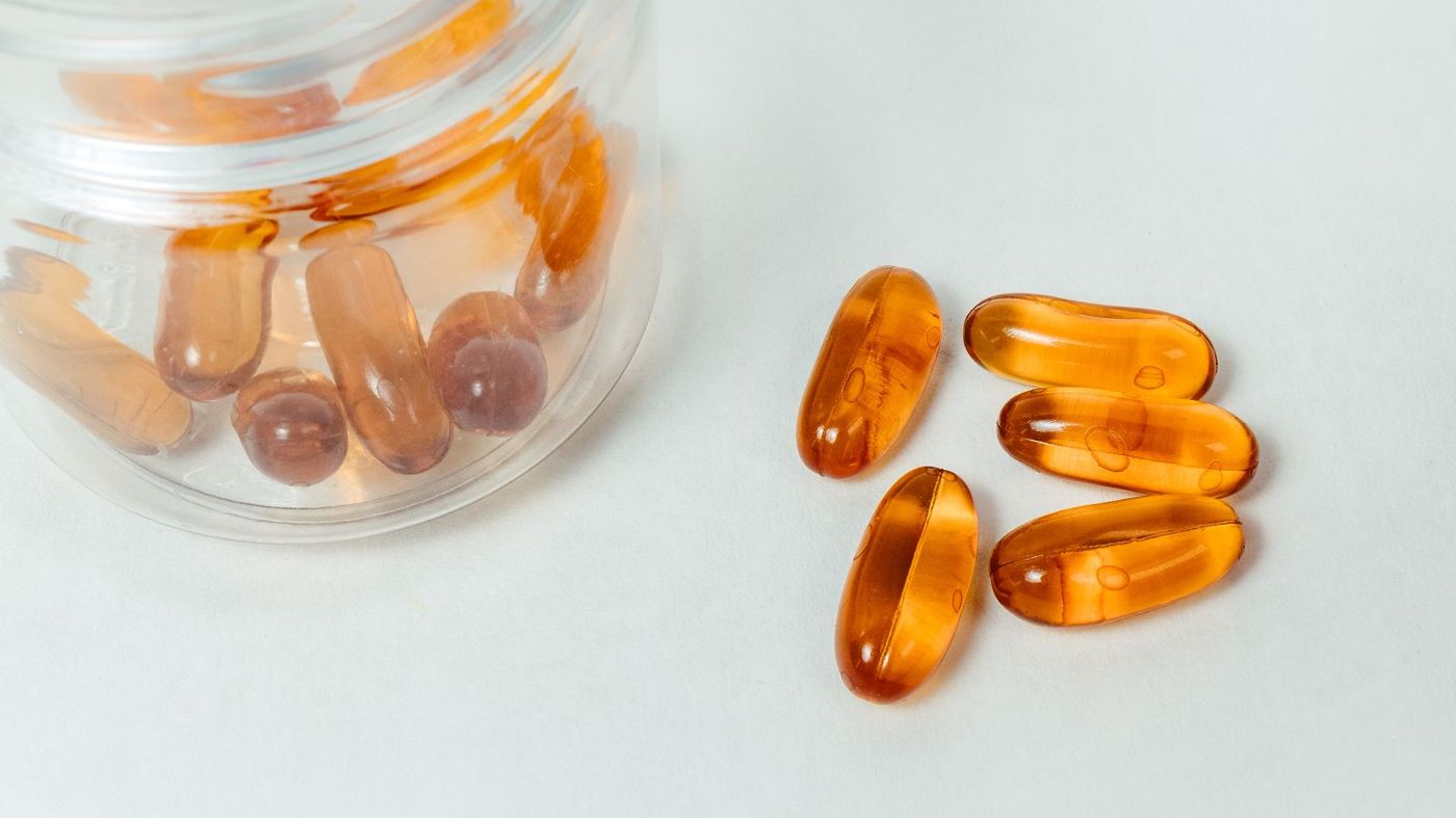 Supplement capsules and a glass jar on a white surface